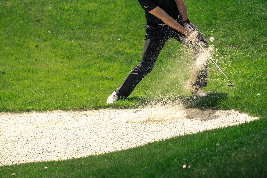 Golfer hitting ball out of the bunker hitting sand into the air