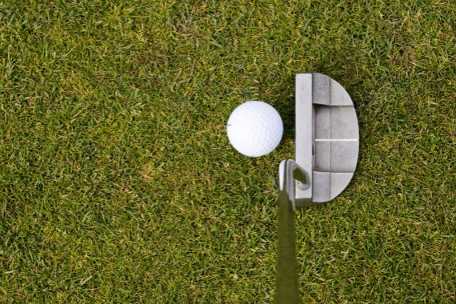 Golf ball near putter on green grass