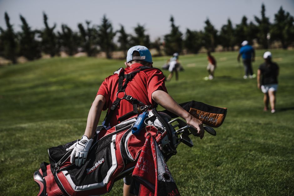 Golfer carrying a red stand bag walking on a golf course
