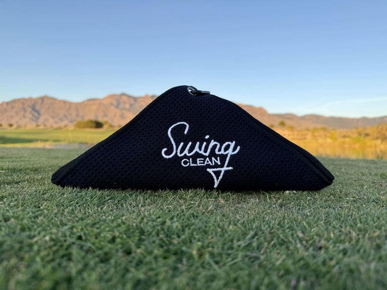 Black Swing Clean Duo Pro waffle golf towel laid on a fairway with mountains behind