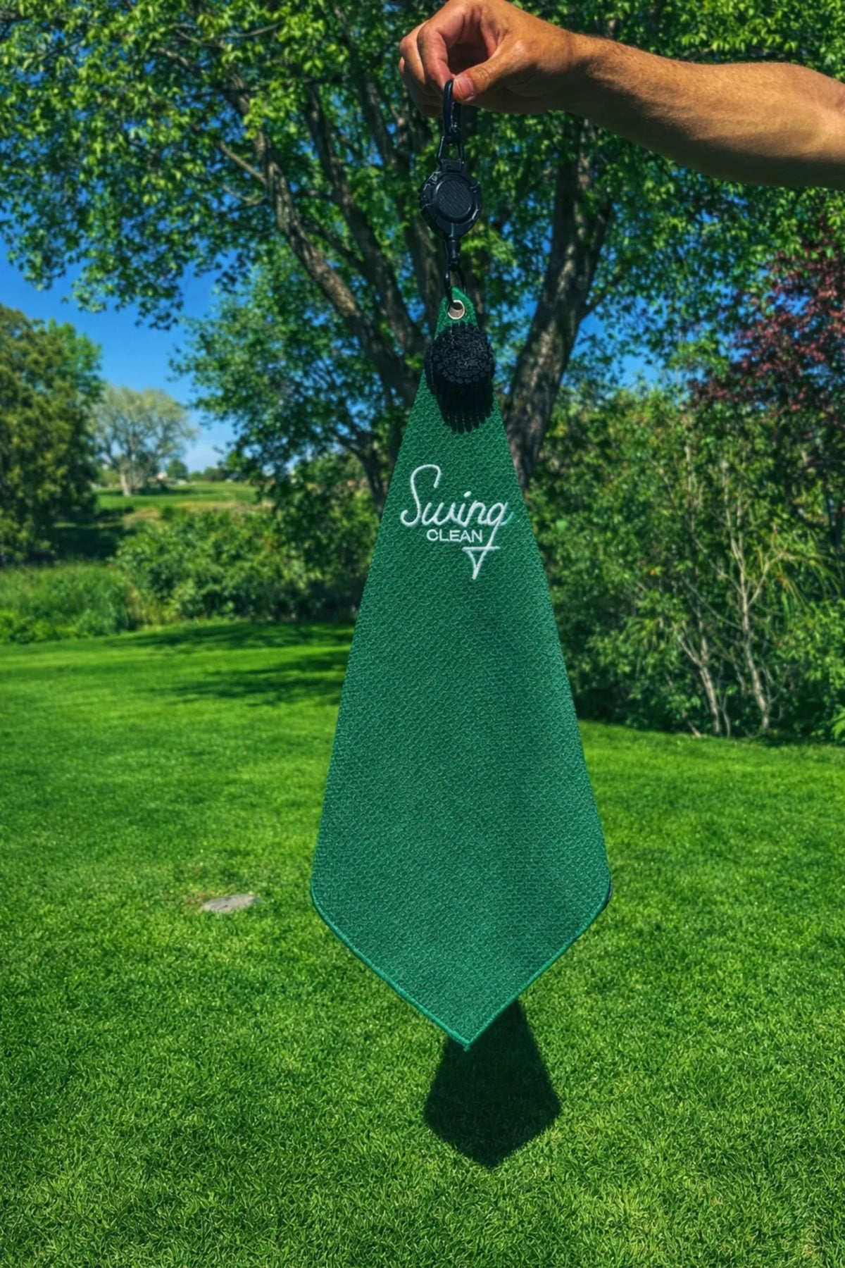 Hand holding up the Bentgrass Green Swing Clean waffle golf towel on the course
