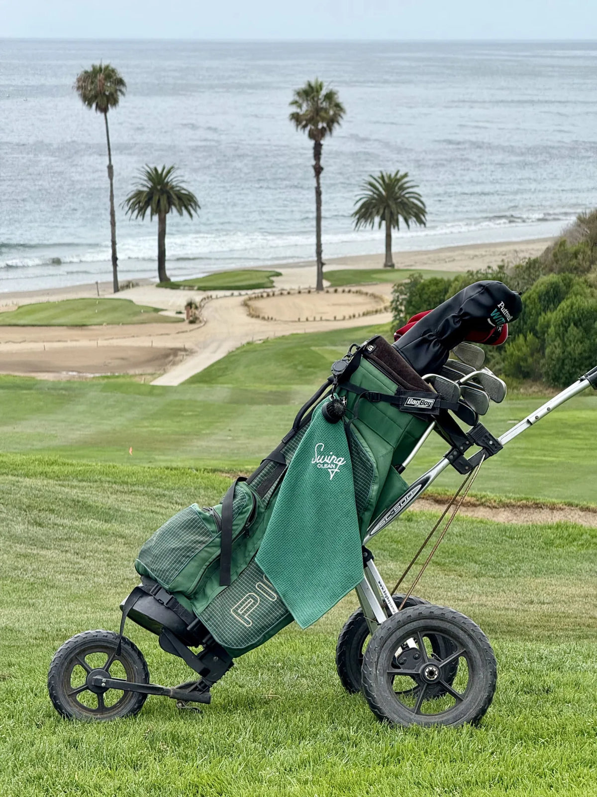 Green Swing Clean Duo Pro towel on a golf push cart overlooking an oceanside fairway