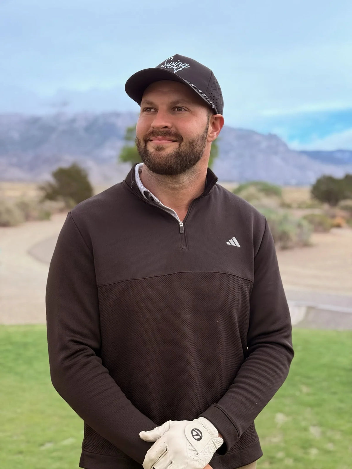 Golfer in a black Swing Clean hat smiling on the course with mountains in the background
